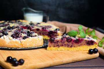 pie with black currant and shortbread, fresh berries. the pie is cut into pieces and the top is sprinkled with powdered sugar . close-up of a piece in the pie section