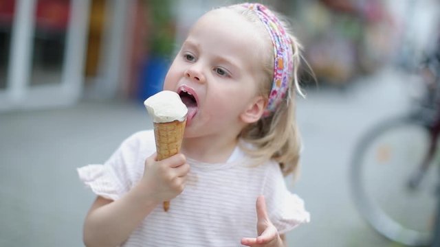 In the city on the street little beautiful girl blonde eats ice cream
