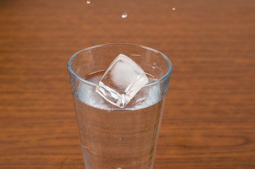A glass and an ice cube on a wooden table
