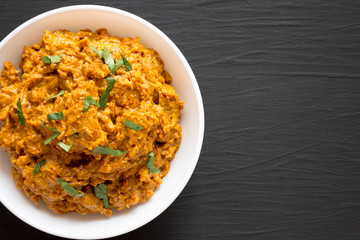 Homemade Chicken Tikka Masala in a white bowl on a black surface, top view. Flat lay, overhead, from above.