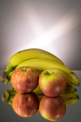 Yellow bananas and red apples on mirroring table. Gorizontal image