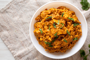 Homemade Chicken Tikka Masala in a white bowl on cloth, top view. Flat lay, overhead, from above. Copy space.