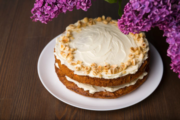 Carrot cake and bouquet of purple lilac on the wooden table