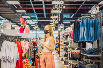 Obraz premium Woman in a clothing store in a medical mask because of a coronovirus. Quarantine is over, now you can go to the clothing store