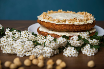 Carrot cake, branch with white flowers and hazel nuts on the wooden table