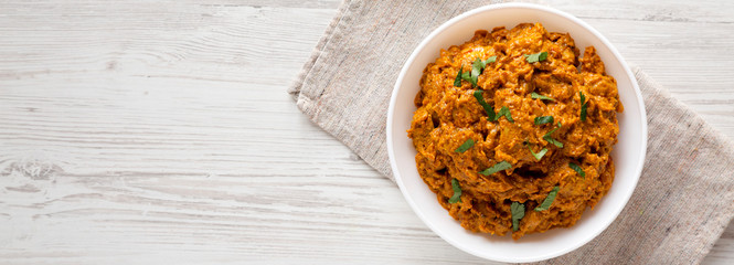 Homemade Chicken Tikka Masala in a white bowl on a white wooden surface, top view. Flat lay, overhead, from above. Space for text.