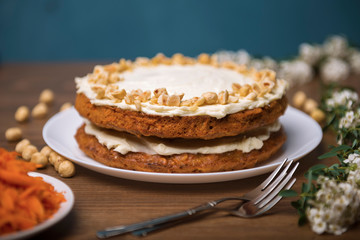 Carrot cake, hazel nuts, grated carrot and branch with white flowers on the wooden table
