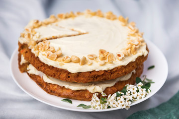 Fototapeta na wymiar Carrot cake with hazel nuts, decorated with white flowers of meadowsweet and slice lemon on the white tablecloth