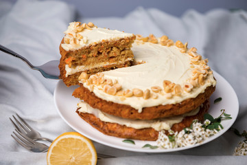 Carrot cake with hazel nuts, decorated with white flowers of meadowsweet and slice lemon on the white tablecloth