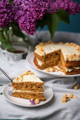 Piece of carrot cake with carrot cake and a cup of tea with bouquet of lilac on the background