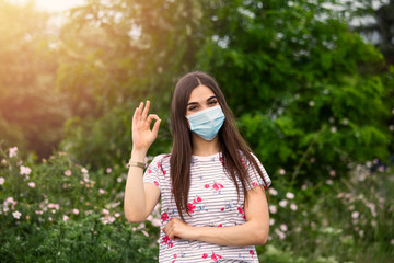 Young woman wearing medical face mask outdoors. Woman Wearing Protective Mask and Showing OK sign. Woman wearing surgical mask for corona virus