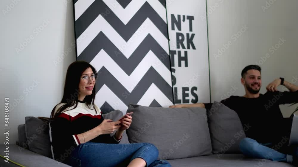 Poster young man sitting on couch with laptop computer and discussing app with girlfriend which chatting in