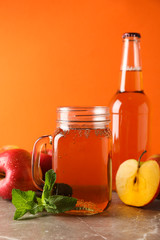 Composition with cider and apples on gray table against orange background
