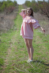 Beautiful blonde woman in pink dress walks through the flowering garden in the spring