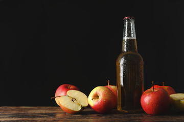 Composition with cider and apples on wooden table against black background