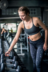 Fototapeta na wymiar Cinematic tone of young attractive fitness woman exercise with dumbbell in gym. Individual sport to fit muscles of body and workout exercise for healthy life concept.