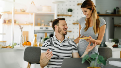 Beautiful wife preparing pancakes for husband. Loving couple enjoying at home.