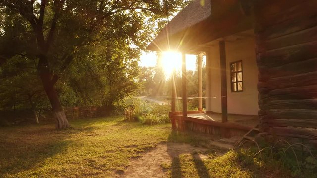 Landscape of old hut house garden and bright sunshine rays. Cabin yard and morning sun.