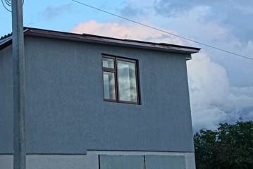 one brown window on the gray concrete wall of a private house against the sky