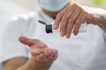 Doctor wearing a surgical mask applying on his hands an antibacterial sanitizer gel, against coronavirus disease (COVID-19). Selective focus