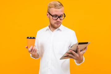 businessman in a white shirt with a tablet and a cup of coffee in hand on a yellow background with copy space