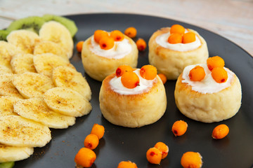 Cheesecakes with sour cream sauce, bananas and sea buckthorn berries