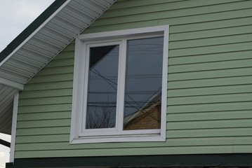 Fototapeta premium attic of a private house with a green plastic wall and one white window on the street