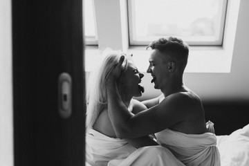 Young man and woman in sheets hug, kiss and laugh. Black and white photo of naked men and women in sheets.