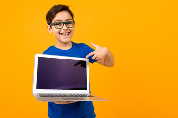 joyful caucasian boy holds laptop screen forward with mock up on yellow studio background with copy...