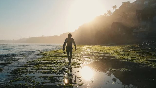 Surfer walking down the reef at sunrise in Bali