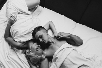 Young man and woman in sheets hug and kiss. Black and white photo of naked men and women in sheets.