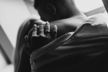 Young man and woman in sheets hug and kiss near the window. Black and white photo of a naked man...
