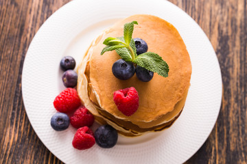 Homemade sweet pancakes with blueberries and raspberries on a white plate, top view.