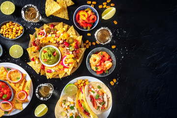 Mexican food, various dishes, shot from the top on a black background with copy space. Nachos, tacos, tequila