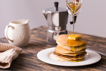 Maple syrup pouring over a stack of mini pancakes.