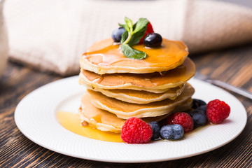 Pancakes with blueberries and raspberry and maple syrup on wooden background. Breakfast and traditional meal.