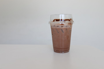CHOCOLATE IN PLASTIC DISPOSABLE CUP for take away on wood counter table in cafeteria on white blurred  background. Close up and selective focus.