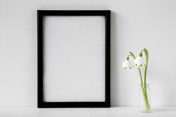 Fresh white snowdrops in glass vase on gray background. Condolence card. Empty place for emotional, sentimental text, quote, sayings or photo in black frame. Front view.