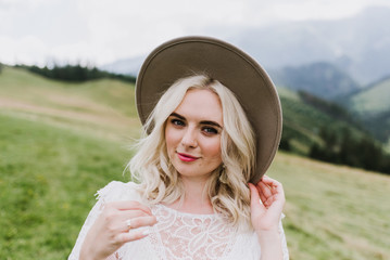 Beautiful bride in a dress in the style of boho walks on the field against the backdrop of the mountains. Wedding photo shoot in the mountains.