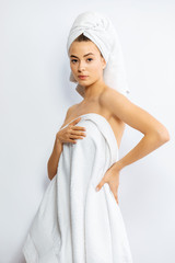 Beautiful young woman wrapped in white bath towel preparing for sauna, studio background