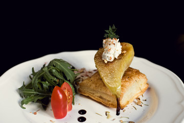 Baked pear with cheese and vegetables close-up in a restaurant.