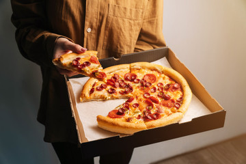 The female hand takes the first new piece of pepperoni pizza out of the delivery box. The concept of fast food