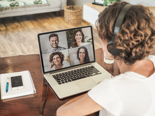 woman having a video conference call with four people at her laptop wearing a headset with notepad...