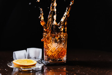 Whiskey with orange and ice close-up. Splashing whiskey in a glass.