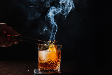 Whiskey with orange, ice and smoking rosemary close-up.
