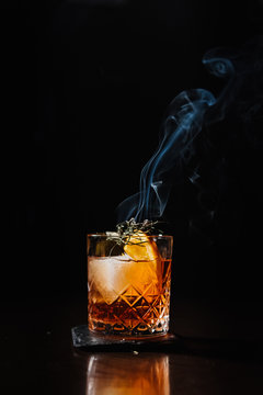 Whiskey with orange, ice and smoking rosemary close-up.
