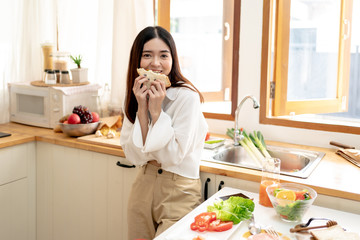 Asian Young Woman Eating Sandwich for Breakfast in the Kitchen.