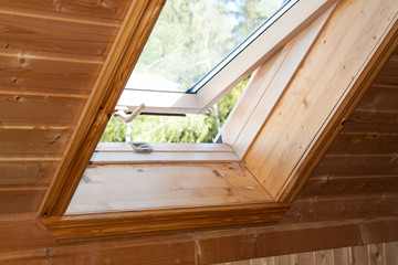 Open dormer window in wooden house in the attic. Room has sloping ceiling made of natural eco-materials and views of park through an open window