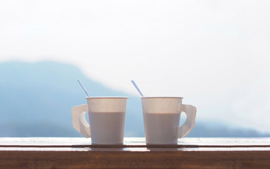 Coffee in a paper cup on a wooden table in the morning with Blurred Mountain background and copy...