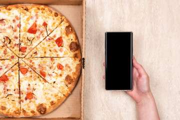 Pizza in a cardboard box and phone in hand on a light marble background. Copy space for your text....